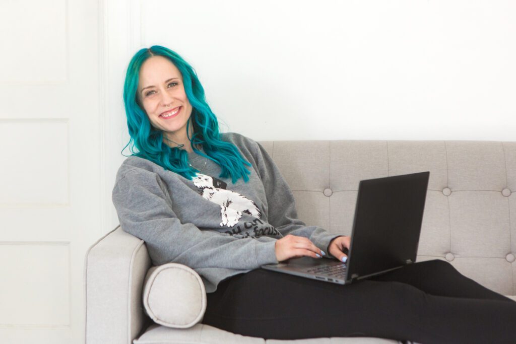 women with blue hair sitting on couch holding laptop